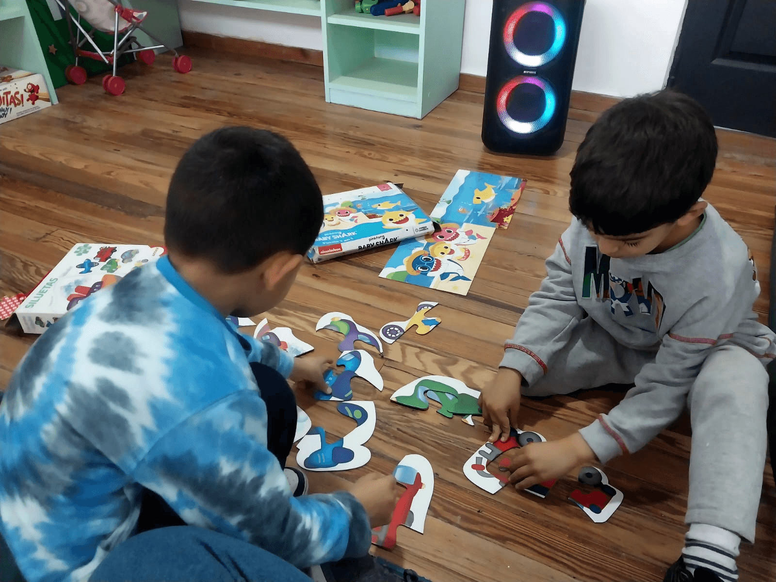 Dos niños armando rompecabezas sentados en el piso de madera.